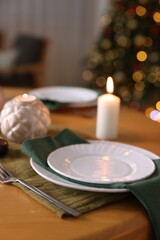 Stylish Christmas table setting with plates, cutlery and burning candles in festive decorated room, closeup. Bokeh effect