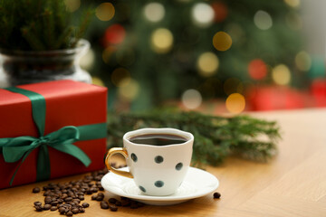 Aromatic coffee in cup, beans and gift box on wooden table against blurred lights, closeup. Space for text