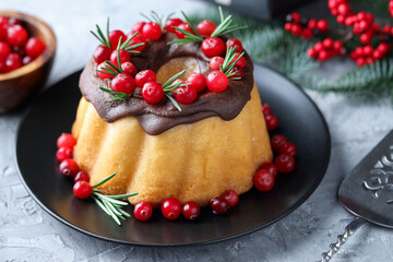 Delicious Christmas cake with chocolate glaze, cranberries and rosemary on grey textured table, closeup