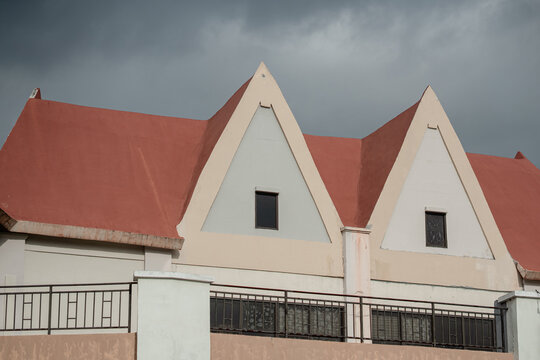 Geometric architectural detail of building tops featuring triangular gables with red and cream colors against a dark contrasting sky.