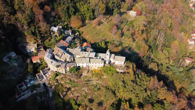 Aerial view of Carmine Superiore, a village with tightly packed stone buildings nestled into the mountainside surrounded by colorful autumn trees, Carmine Superiore, Piedmont, Italy.