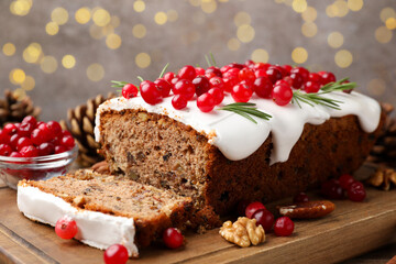 Tasty Christmas cake with icing, cranberries and rosemary on wooden table against background with blurred lights, closeup