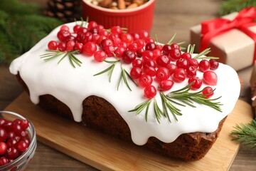 Tasty Christmas cake with icing, cranberries, rosemary and festive decor on wooden table, closeup