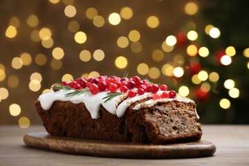 Tasty Christmas cake with icing, cranberries and rosemary on wooden table against background with blurred lights, closeup