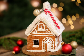 Beautiful gingerbread house and ornaments on wooden table against blurred lights, closeup. Christmas treat