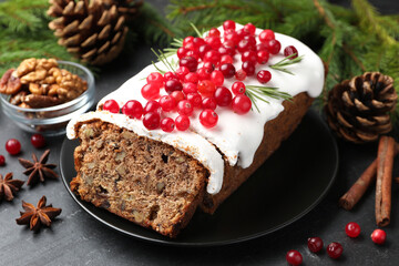 Tasty Christmas cake with icing, cranberries and festive decor on black table, closeup