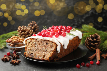 Tasty Christmas cake with icing, cranberries and festive decor on black table against blurred lights, closeup. Bokeh effect