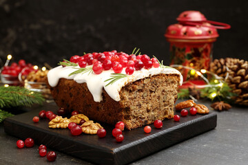 Tasty Christmas cake with icing, cranberries, nuts and festive decor on black table, closeup
