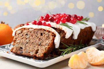 Tasty Christmas cake with icing, cranberries and tangerines on light grey table against blurred lights, closeup. Bokeh effect
