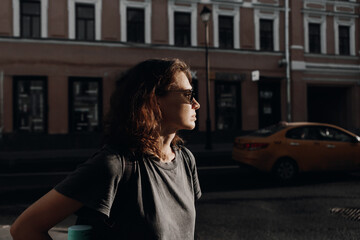 A profile of a young woman traveling on a city street. Houses and a taxi are in the background....