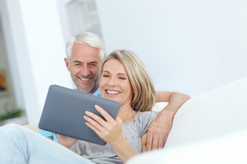 Mature couple, tablet and smile on sofa with love, bonding or healthy relationship in home. Man, woman and technology in living room with movie, video and social media together for weekend break