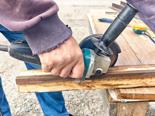 Worker using an angle grinder on wood at a construction site during daytime