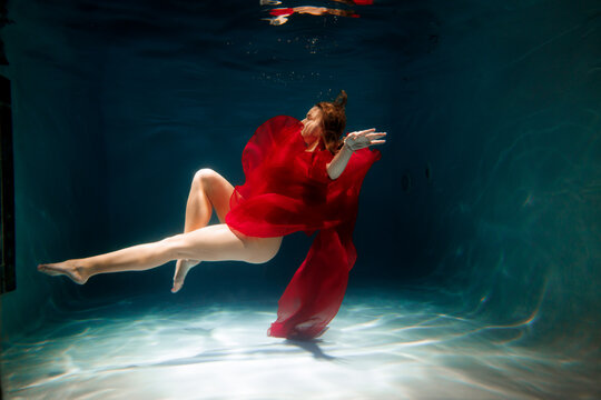 white synchronized swimmer practicing underwater in red dress