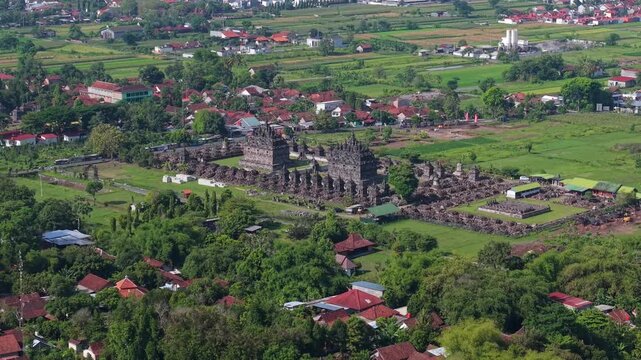Aerial view of the ancient Candi Plaosan temple complex, amidst lush green trees and scattered houses, creating a vibrant contrast, Klaten Regency, Jawa Tengah, Indonesia.