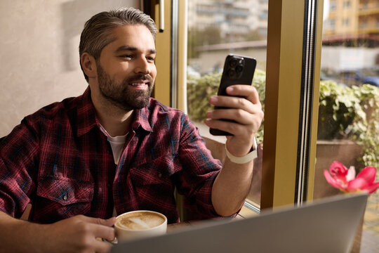 Mature handsome man enjoying coffee while browsing on his smartphone at a cozy cafe