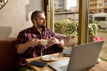 Mature man in stylish outfit enjoys coffee while working in a cozy cafe