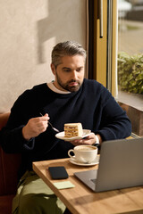 Charming man enjoys dessert while working on laptop in cozy cafe setting