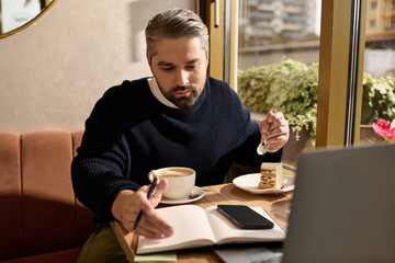 Mature man enjoying coffee and dessert while engaged in creative writing at cozy cafe