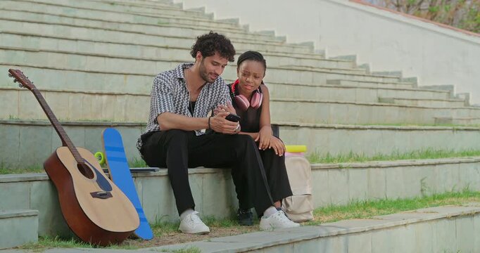 Indian young adult gen z woman lady male man sitting stair use mobile look screen check online work do e chat place. Happy boy girl hold phone watch video talk share gossip enjoy day spend break time