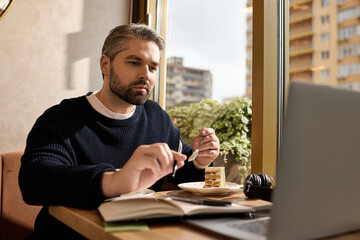 Mature man enjoying dessert while working on a laptop at a cozy cafe