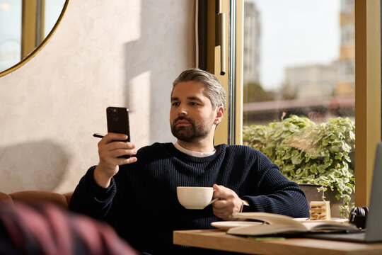 Handsome mature man enjoys coffee while engaging with his phone in a cozy cafe setting