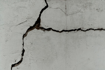 Severe diagonal crack fracturing a rough white concrete wall, depicting structural damage, earthquake effect, aging, and decay texture.