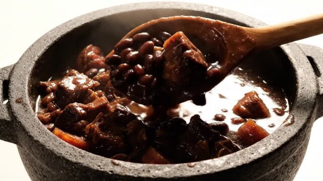 Wooden Spoon Stirring Delicious Feijoada in an Inviting Stone Pot on a White Background