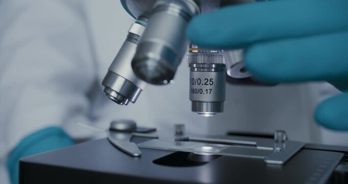 Detailed macro of gloved hands adjusting laboratory microscope for analysis