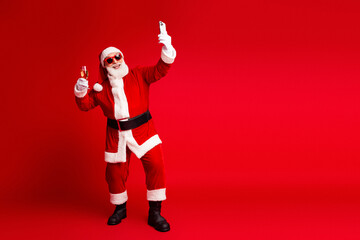 Santa takes selfie with champagne in hand posing for festive photo against bold red background