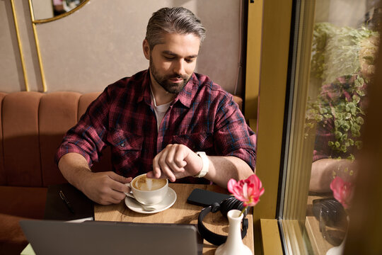 Stylish mature man enjoys coffee while checking the time at a cozy cafe
