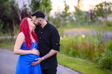 A couple kisses during a walk, the man gently holding the pregnant woman’s belly. A warm moment of love and expecting a baby, surrounded by nature and soft evening light