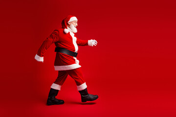 Santa in red suit walking on a bold red background delivering festive mood for christmas and...