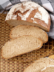 A loaf of sliced bread. Two slices are in front, and the loaf is behind them with a checkered cloth in the background.