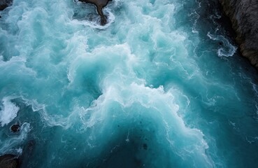 Aerial view of Bruarfoss waterfall in Iceland. Blue water flows between rocky cliffs. Whitewater rapids visible from above. Turquoise river flows through narrow passage. Waterfall landscape in early