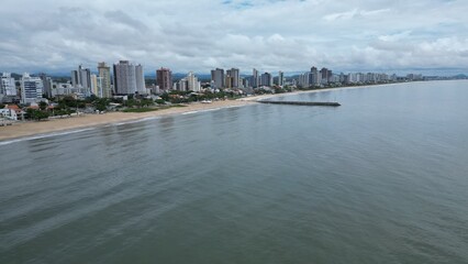 Aerial shot of a long pier jutting into a calm, gray sea under a cloudy sky. Unidentifiable people stand at the end, with distant islands on the horizon. Peaceful, minimalist coastal scene.