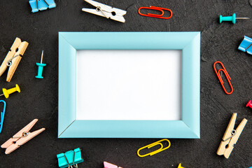 A light blue empty picture frame surrounded by colorful office supplies on a dark textured background