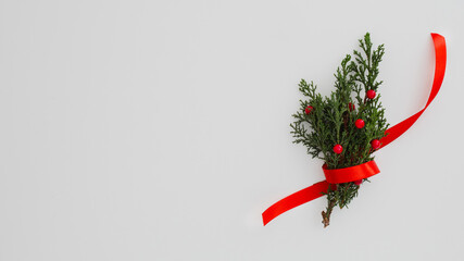 A small evergreen sprig with red berries tied with a festive red ribbon on a plain background