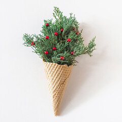 A creative arrangement of greenery and red berries presented in a waffle cone