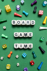 Wooden dice show the phrase 'Board Game Time' with a selection of colourful dice and game tokens lying around it on a vibrant green baize fabric