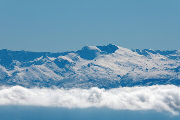 The iconic Mulhac n and Veleta peaks of Sierra Nevada emerge snow-covered above a soft blanket of clouds, under a clear blue sky, capturing Spain s highest summits in winter.