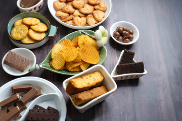 Assorted party snacks on table featuring chocolate cream sandwich biscuits, sugar coated heart cookies, wafer chocolates, chocolate coated caramel balls, salted crackers, and crispy potato chips.
