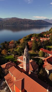 Cinematic drone flight over Lake Como framed by autumn-winter mountains and a red-tiled Italian village, with a tall historic bell tower rising above the rooftops