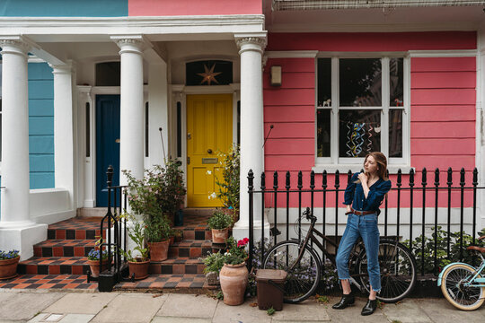 A young woman stands by a bicycle in front of a colorful row of houses in London Borough of Camden.