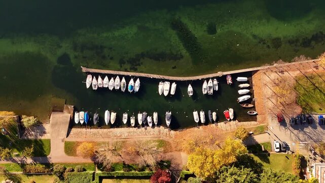 Aerial drone flight over a marina on Lake Como with boats moored along the waterfront, surrounded by alpine scenery and reflective waters in a cinematic lakeside view