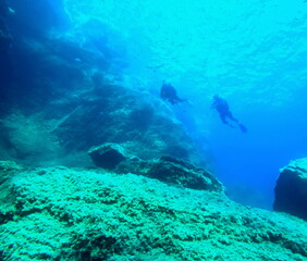 two divers beginning the dive, near sea surface in mediterranea, seen from under the water