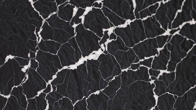 Cracked black surface texture with white lines, abstract pattern background resembling marble or dried earth, modern dramatic effect for elegant
