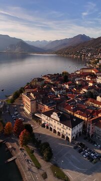 Cinematic aerial orbit of a Lake Maggiore village with red rooftops, autumn mountains and serene lakeside views, capturing the warm and atmospheric essence of northern Italy