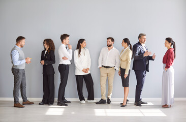 A diverse group of professionals stands and interacts in a well-lit modern office space. They are engaged in conversation, showcasing teamwork and collaboration.