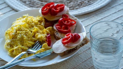 Scrambled eggs and open sandwiches with pepper and poultry on breakfast plate
