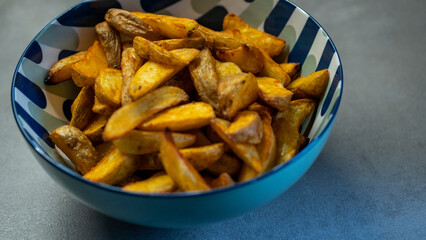 Crispy homemade potato wedges in decorative bowl on kitchen counter